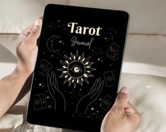 May include: A black tablet displaying a "Tarot Journal" design. The design features a sun with an eye, hands, a crescent moon, stars, and tarot card illustrations in a gold color. The tablet is held by two hands.