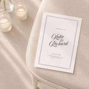 May include: A white rectangular wedding invitation card featuring a black scalloped border. The text reads: THE WEDDING OF Katie & Richard 05.02.2028 STONES OF THE YARRA VALLEY VICTORIA, AUSTRALIA. The card is printed in black ink on a smooth white paper stock.