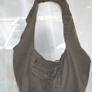 May include: A large, grey canvas tote bag with a zipped pocket and a flap pocket. The bag is hanging on a hanger.