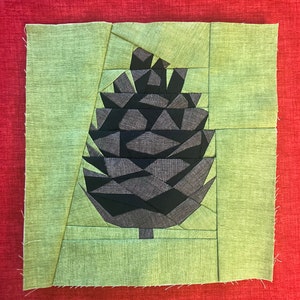 May include: A green fabric square with a black and grey geometric pine cone design in the centre.