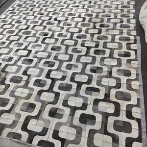 Alfombra de piel de vaca con diseño de patchwork y correas, color gris y blanco.