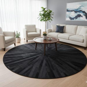Op de afbeelding: Een groot, rond zwart tapijt met een sunburst-ontwerp domineert de woonkamer. Het tapijt is gemaakt van donkergrijze en zwarte rechthoekige stukken. De kamer heeft ook een witte bank, twee fauteuils, een houten salontafel en een plant in een pot.