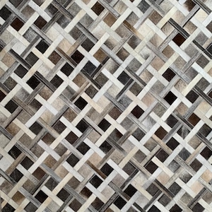 May include: A woven rug with a geometric pattern. The rug features a mix of neutral colors, including shades of brown, gray, and cream. The design is a repeating pattern of interwoven strips, creating a textured surface. The rug is likely made of natural materials.