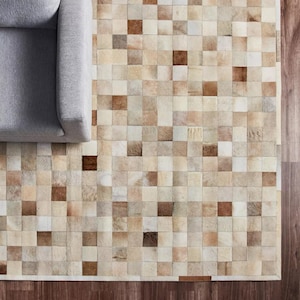 May include: A rectangular area rug composed of small, square-shaped patches in varying shades of cream, beige, tan, and brown. The rug features a grid-like pattern of natural hide textures, positioned partially beneath a grey upholstered chair.