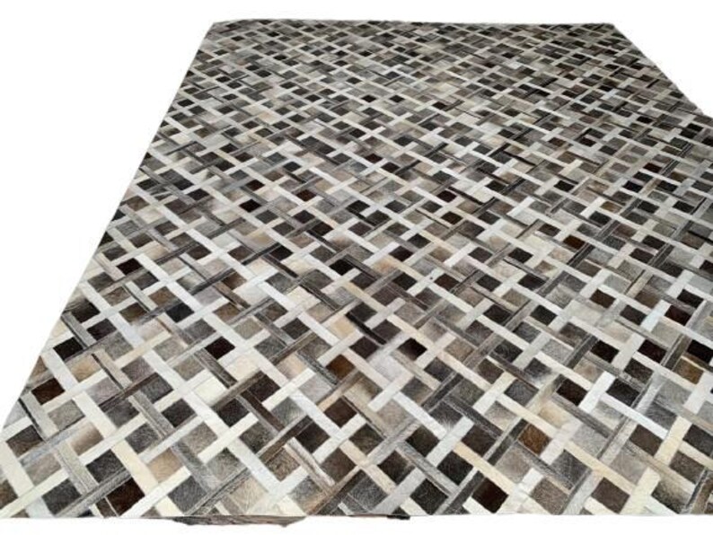 May include: A large, rectangular rug with a woven pattern. The rug features a mix of neutral colors, including white, beige, gray, and brown. The design is a repeating geometric pattern, creating a textured appearance.