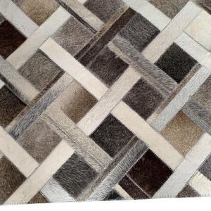May include: A rectangular rug with a patchwork design. The rug features a geometric pattern of squares and rectangles in shades of brown, beige, gray, and white. The texture appears to be a mix of materials, possibly leather or hide.