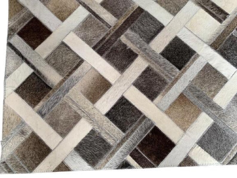 May include: A rectangular rug with a patchwork design. The rug features a geometric pattern of squares and rectangles in shades of brown, beige, gray, and white. The texture appears to be a mix of materials, possibly leather or hide.