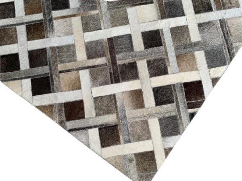 May include: A geometric rug with a patchwork design. The rug features a pattern of intersecting rectangles in shades of brown, gray, and cream. The texture appears to be soft and the rug is likely made of natural materials.