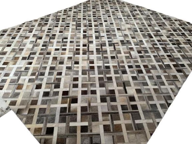 May include: A large, rectangular rug with a woven pattern. The rug features a patchwork design with squares and rectangles in shades of brown, gray, and cream. The texture appears to be soft and inviting, suitable for a living room or bedroom.