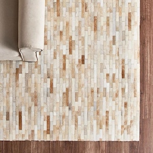 May include: A rectangular area rug composed of numerous vertical, narrow strips of hide in varying shades of cream, beige, tan, and light brown. The strips are arranged in a staggered, brick-like pattern, creating a textured surface.
