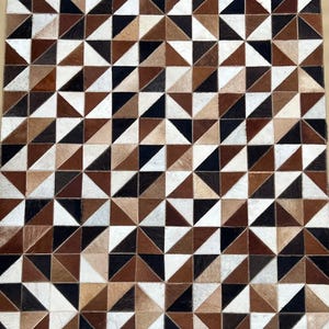 Könnte beinhalten: Ein geometrischer Kuhfellteppich mit einem sich wiederholenden Dreiecksmuster in Braun-, Schwarz- und Weißtönen. Das Design des Teppichs erzeugt einen visuell ansprechenden Mosaikeffekt, der sich eignet, jedem Raum einen rustikalen Touch zu verleihen.