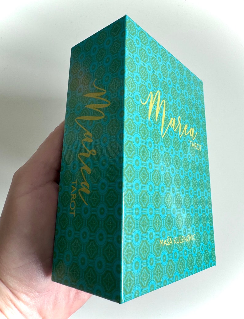 May include: A teal green box with a gold geometric pattern and the text "Marcea Tarot" in gold lettering. The box is designed by Masa Kulenović.