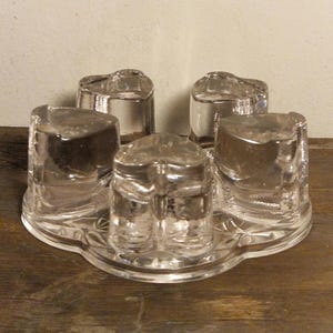 May include: A clear glass candle holder with four heart-shaped candle cups and a decorative base.