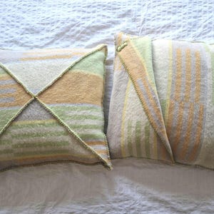 Può includere: Due cuscini decorativi con un motivo a righe in tonalità di verde, giallo e bianco. I cuscini sono realizzati in un tessuto morbido e testurizzato.