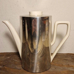 May include: A white ceramic coffee pot with a silver metal body and a white lid. The pot has a spout and a handle.