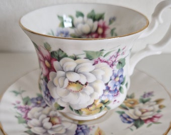 May include: A white teacup and saucer with a floral pattern. The cup and saucer have a gold trim. The flowers are pink, purple, blue, and yellow.