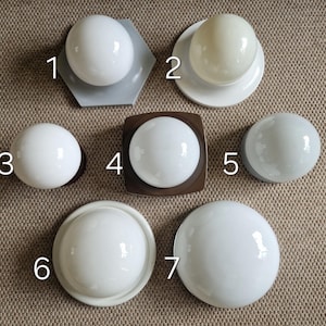 May include: Seven white globe-shaped light fixtures with various base designs. The bases include a grey hexagon, a white circle, a brown square, and a grey half-circle. The globes are made of opaque glass, suitable for interior lighting.