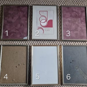 May include: A collection of six rectangular picture frames with metallic gold-colored borders. The frames contain various colored backgrounds, including burgundy, white, and gray. One frame features a print with red and white abstract shapes and text.