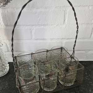 May include: A vintage wire drink caddy with a handle, holding six clear glass tumblers with a diamond pattern.