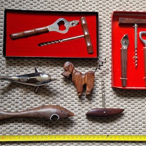 May include: A set of five bottle openers, including a dolphin-shaped opener, a wooden fish-shaped opener, a wooden dog-shaped opener, and two sets of bottle openers in red boxes.