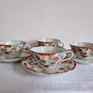 May include: Set of four white teacups and saucers with a floral pattern in shades of red, blue, green, and brown. The cups and saucers have a scalloped edge.