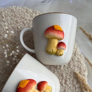 以下が含まれることがあります： 赤、黄色、オレンジ色の彫刻されたキノコが特徴の、茶色の縁が付いたクリーム色のセラミックマグ。 マグカップには湾曲したハンドルと斑点のある仕上げが施されています。 デザインはあなたのキッチンに自然のタッチを追加します。