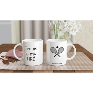 Puede incluir: Dos tazas de cerámica blanca con texto negro y un diseño de raqueta de tenis. La taza de la izquierda dice "Tennis is my HRE". La taza de la derecha dice "Happy Relaxed Engaged" y tiene un diseño de raqueta de tenis y pelota.
