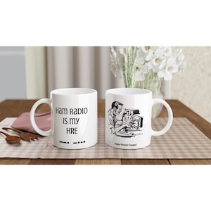 Puede incluir: Taza de cerámica blanca con una ilustración negra de una persona usando una radioaficionado y el texto "Ham Radio is my HRE" y código morse.