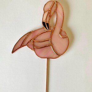 Puede incluir: Un flamenco de vidrio rosado con detalles de alambre de cobre. El flamenco está posado sobre un tallo de alambre de cobre.