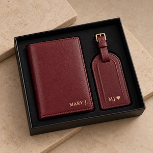 May include: A dark red passport holder and a matching luggage tag set presented in a black gift box. The passport holder is embossed with the text MARY J. and the luggage tag features the initials MJ followed by a small heart symbol in gold.