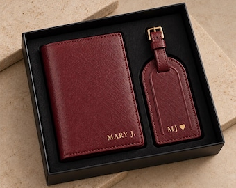 Può includere: Un portapassaporto e un'etichetta per bagagli abbinata di colore rosso scuro presentati in una scatola nera. Il portapassaporto è impresso con il testo MARY J. e l'etichetta mostra le iniziali MJ seguite da un piccolo cuore in oro.