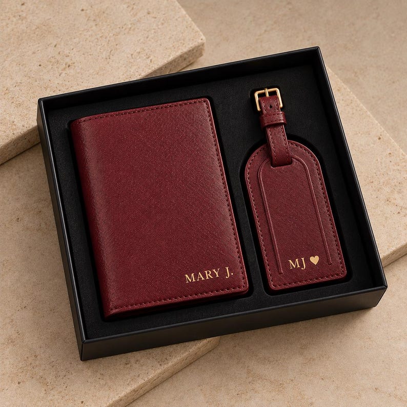 May include: A dark red passport holder and a matching luggage tag set presented in a black gift box. The passport holder is embossed with the text MARY J. and the luggage tag features the initials MJ followed by a small heart symbol in gold.