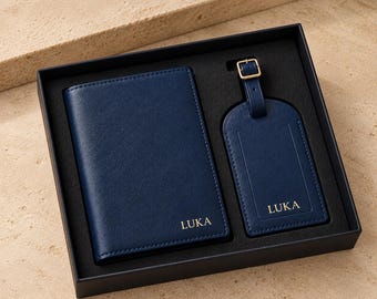 May include: A navy blue passport holder and a matching luggage tag set presented in a black gift box. Both items feature the name LUKA embossed in gold lettering. The luggage tag includes a gold-toned metal buckle strap for secure attachment.