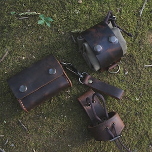 May include: Three leather pouches with metal hardware and a canvas pouch. The pouches are brown and have a distressed look. The canvas pouch is beige and has a brown leather strap.