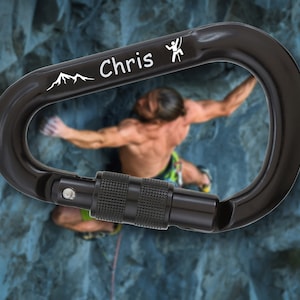 Peut inclure: Un mousqueton noir avec une inscription argentée qui dit "Chris" et un graphique de chaîne de montagnes. Une petite icône de grimpeur est également gravée sur le mousqueton.