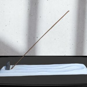 Peut inclure: Porte-encens en céramique blanche avec un design ondulé. Un bâtonnet d'encens en bois est placé dans le porte-encens.