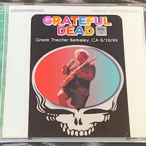 May include: A CD case with a colorful image of a Grateful Dead concert. The case features the band's name in a psychedelic font and the text "Greek Theater Berkeley, CA 6/16/85".