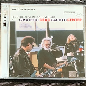 May include: A CD case featuring a live performance by the Grateful Dead at the Capitol Center in Landover, MD. The cover includes a band photo and text that reads "Grateful Dead Capitol Center" in red and white. The case is labeled "2 DISCS".