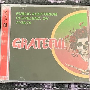 May include: A CD case with a black background and a red circle with a skull and flowers. The text "GRATEFUL" is in large, white letters. The text "PUBLIC AUDITORIUM CLEVELAND, OH 11/29/79" is in white letters at the top of the case.