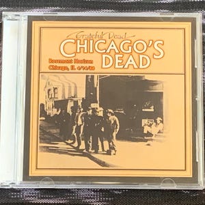 May include: A clear plastic CD jewel case containing a music album titled Grateful Dead Chicago's Dead. The cover features a sepia-toned photograph of people standing outside the Rosemont Horizon in Chicago, IL, dated 4/14/88, with bold text.