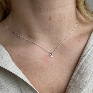 May include: A silver chain necklace with a small silver pendant in the shape of the letter E.