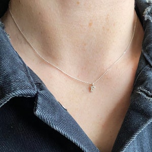 May include: A silver chain necklace with a small letter 'F' pendant. The necklace is worn by a person wearing a black denim jacket.