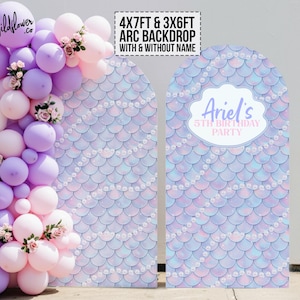Puede incluir: Un telón de fondo con temática de sirena para una fiesta de cumpleaños. El telón de fondo es de color azul claro y morado con un patrón de escamas y detalles de perlas blancas. El telón de fondo está disponible en dos tamaños: 4x7 pies y 3x6 pies. El telón de fondo se puede personalizar con un nombre, como se muestra en la imagen, o sin nombre.