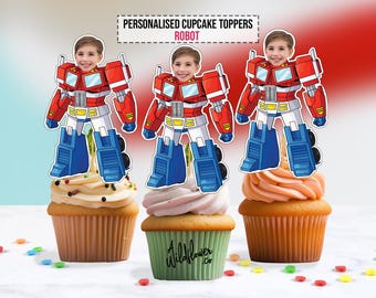 May include: Three cupcakes topped with personalized robot-themed toppers. The toppers feature a child's face on a red, white, and blue robot design. The cupcakes have different colored frosting and are decorated with sprinkles.