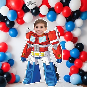 May include: A child's face is visible in a cardboard cutout of Optimus Prime, surrounded by a balloon arch. The balloons are red, white, blue, and black. The Wildflower.co logo is on a white balloon.