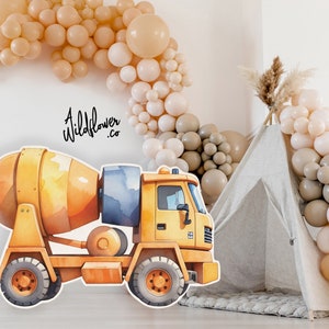 Puede incluir: Un recorte de camión mezclador de cemento de acuarela amarillo y azul. El camión está delante de una tienda de campaña tipi y una pared decorada con un arco de globos en tonos beige y blanco. El texto "A Wildflower.co" está escrito en la pared.