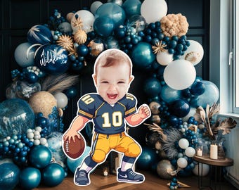 May include: A smiling baby wearing a football uniform, holding a football, and standing in front of a balloon arch. The arch features various shades of blue and white balloons, with the text "Wildflower .co" on one of the balloons.