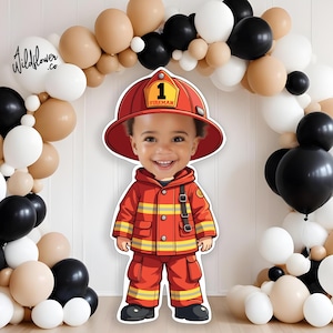 Puede incluir: Un recorte de cartón de un niño vestido de bombero. El niño lleva un traje de bombero rojo con rayas amarillas y un cinturón negro. El niño sostiene una manguera de incendios roja. El niño sonríe y lleva un casco de bombero rojo en la cabeza. El casco tiene el número "1" y la palabra "Bombero" en él. El recorte está delante de un arco de globos hecho de globos blancos, negros y marrones.
