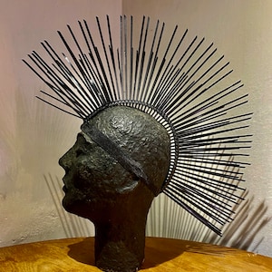 May include: A black headpiece with a large, spiky design made of thin, black strips. The headpiece is worn on a black mannequin head.