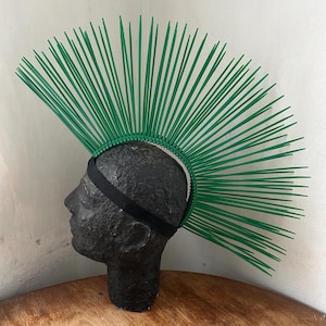 May include: A green mohawk headpiece made of thin plastic strips. The headpiece is worn on a black mannequin head.